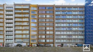 A multi-story residential building with balconies, a parking area with cars, and a construction site on the right. - Apartment by the Sea near Marina (BLANKENBERGE)
