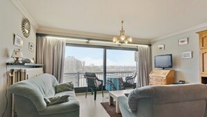 Een woonkamer met twee banken, een salontafel, een televisie en een uitzicht op een stadsgezicht door grote ramen.
