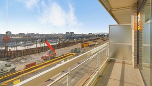 A construction site with cranes and vehicles, a waterfront view, and a building with a balcony. - Apartment in Blankenberge near Belgium Pier (BLANKENBERGE)
