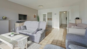 A living room with a grey sofa, a coffee table, and a TV. There is a kitchen area in the background. - Apartment in Blankenberge near Belgium Pier (BLANKENBERGE)