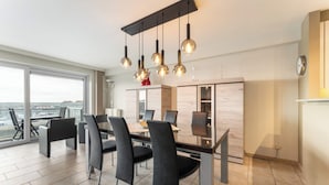 A modern dining area with a large table and chairs, a view of the sea through large windows, and pendant lighting. - Apartment in Blankenberge near Belgium Pier (BLANKENBERGE)