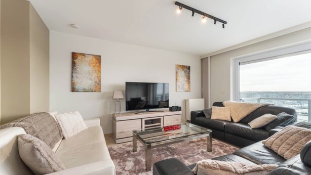 A modern living room with a sofa, a coffee table, a TV, and artwork on the walls. - Apartment in Blankenberge near Belgium Pier (BLANKENBERGE)