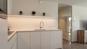 Una cocina moderna con armarios blancos, un lavamanos de acero inoxidable y tres macetas con plantas sobre un estante flotante.