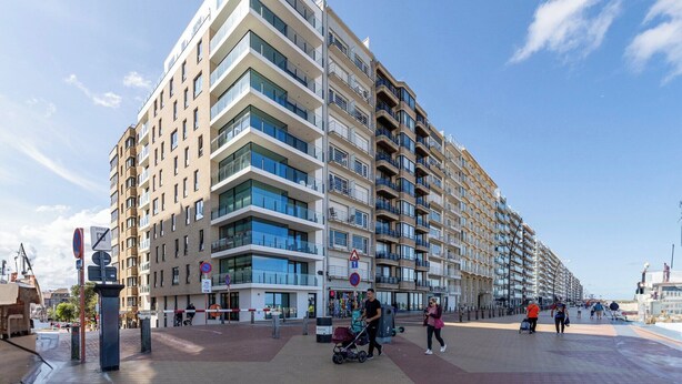 Un edificio residencial de varios pisos con balcones, un paseo peatonal y cielos despejados.