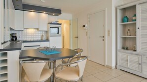 A modern kitchen with a built-in oven, a coffee machine, and a dining area with a table and chairs. - Apartment in Blankenberge near Belgium Pier (BLANKENBERGE)