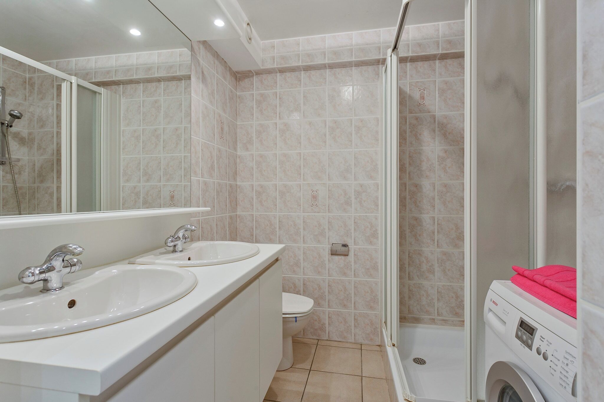 Un baño con dos lavamanos, un inodoro, una ducha y una lavadora.