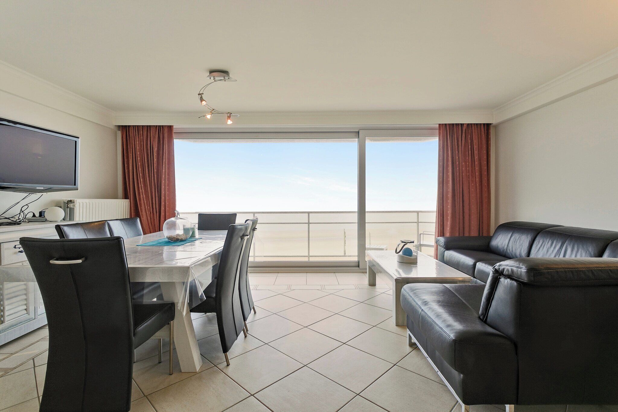 A modern hotel room with a dining area, a sofa, a TV, and a balcony with a view.