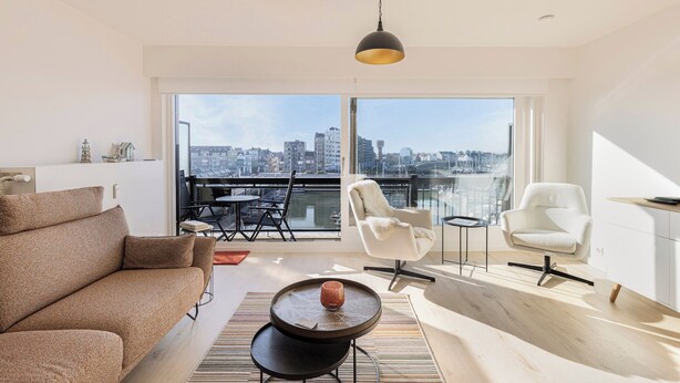 Una sala de estar moderna con un ventanal grande, un sofá, un sillón, una mesita de centro y una lámpara colgante.