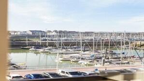 Un puerto deportivo con numerosos barcos amarrados, un puente al fondo y un cielo despejado.