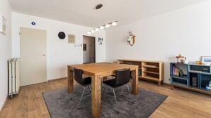 A room with a wooden dining table, two chairs, a radiator, a grey rug, a bookshelf, and a mounted animal head on the wall.