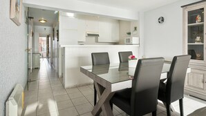 Una cocina moderna con armarios blancos, una isla central y una zona de comedor con mesa de vidrio y sillas negras.