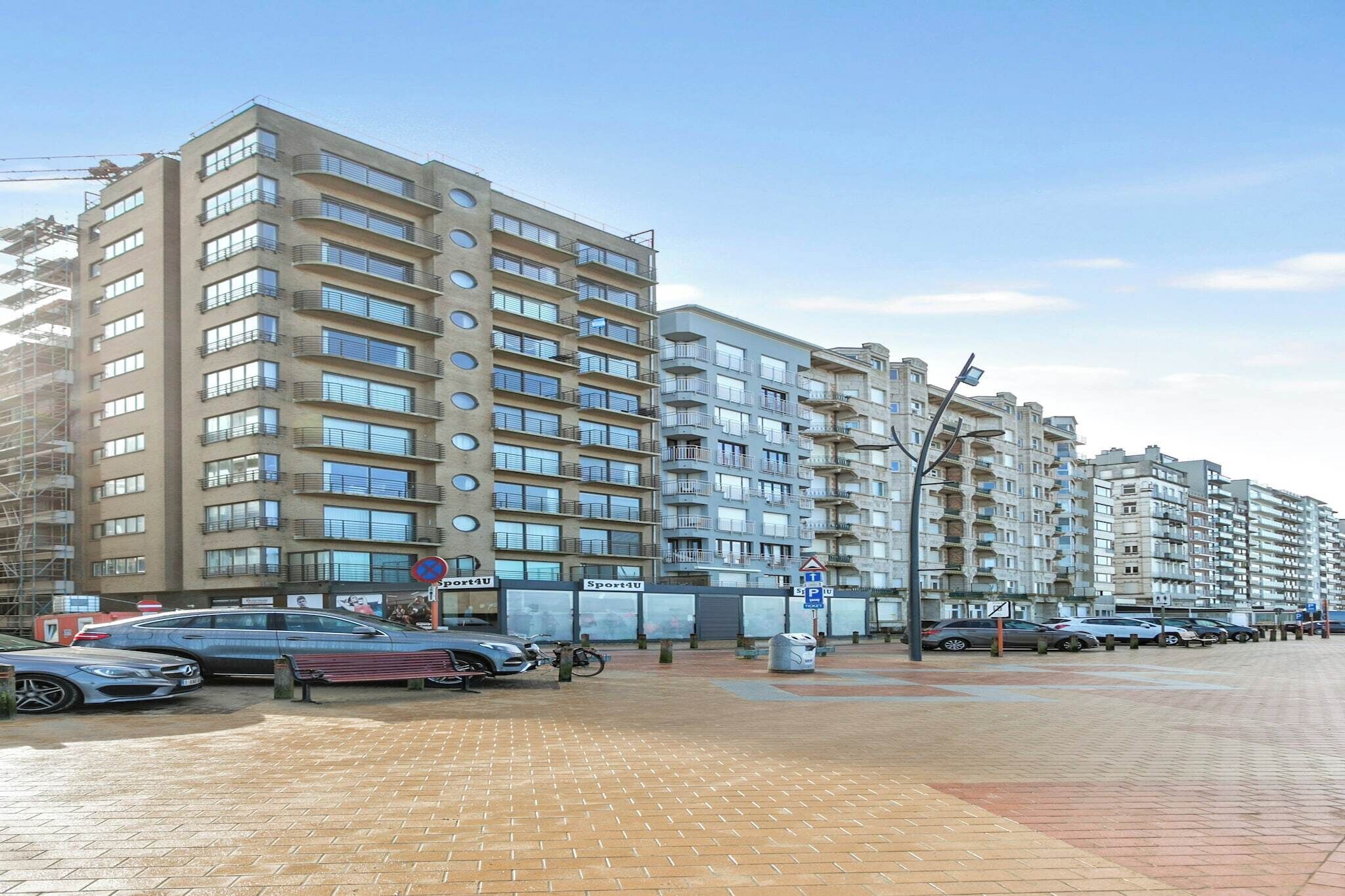 Un edificio residencial de varios pisos con balcones, un estacionamiento con coches y un cielo despejado.