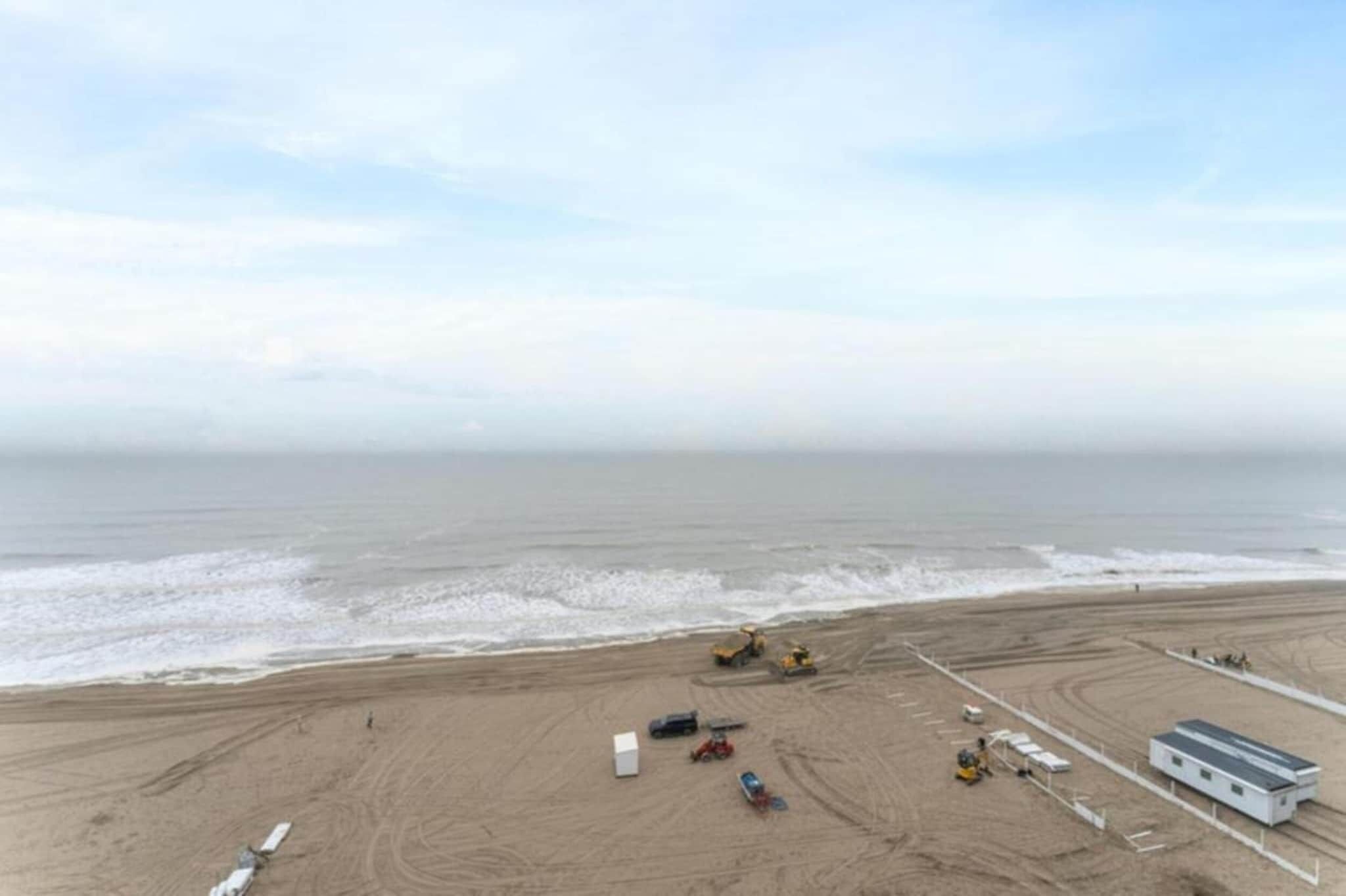 An aerial view of a beach with construction equipment, a small building, and a fenced area.