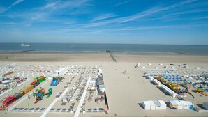 A beach with numerous beach umbrellas and sun loungers, a water slide, and a lifeguard tower. - Apartment in Blankenberge with Sea Views (BLANKENBERGE)