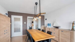 A modern kitchen with a wooden table, black chairs, and a hanging light fixture. - Apartment in Blankenberge with Sea Views (BLANKENBERGE)