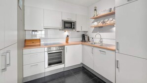 A modern kitchen with white cabinets, a microwave, a coffee maker, and a wooden countertop. - Apartment in Blankenberge with Sea Views (BLANKENBERGE)