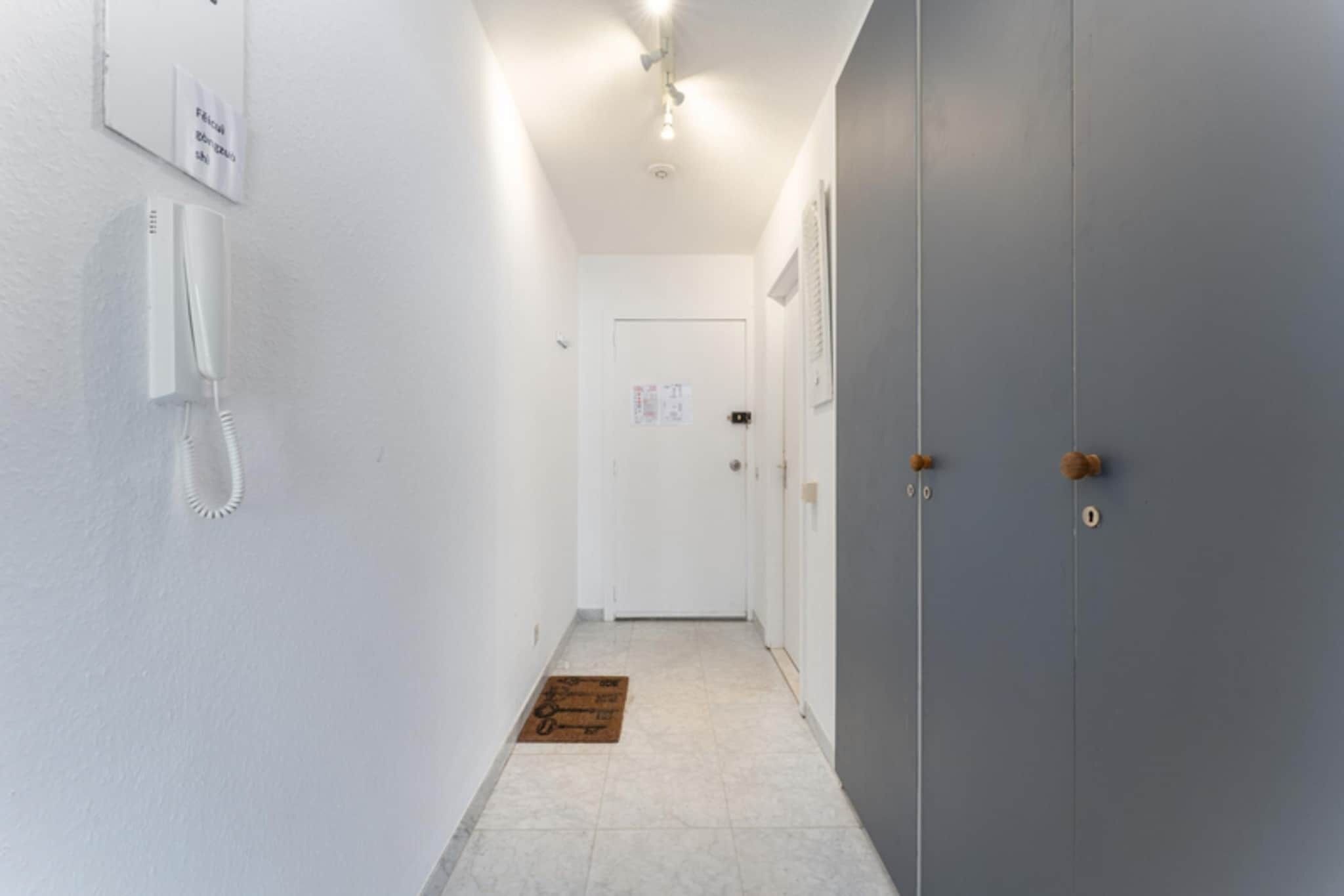 A narrow hallway with a white wall, a door with a doorknob, and a wall-mounted telephone.