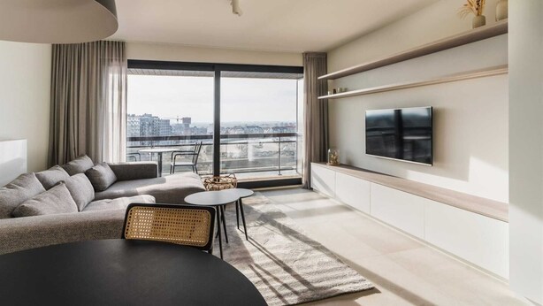 A modern living room with a large window, a sofa, a TV, and a dining area.