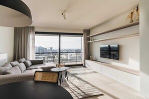 Ein modernes Wohnzimmer mit großem Fenster, einer Couch, einem Fernseher und einem Essbereich.