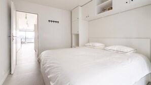 A minimalist bedroom with a large bed, white walls, and built-in storage.