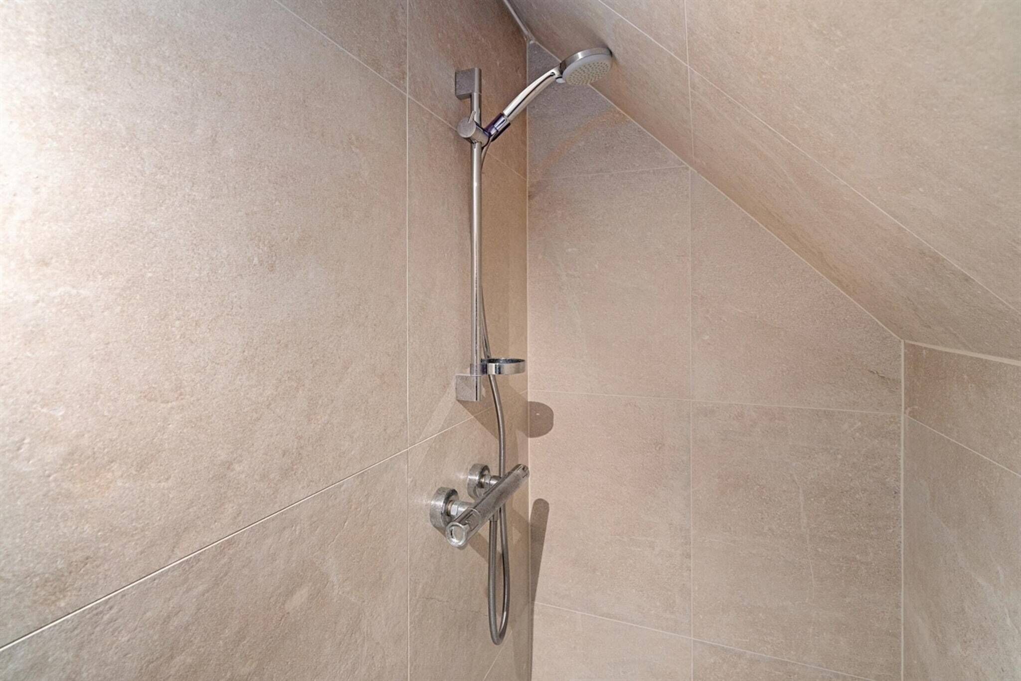 A shower with a handheld showerhead and a wall-mounted control panel in a bathroom with beige tiles.