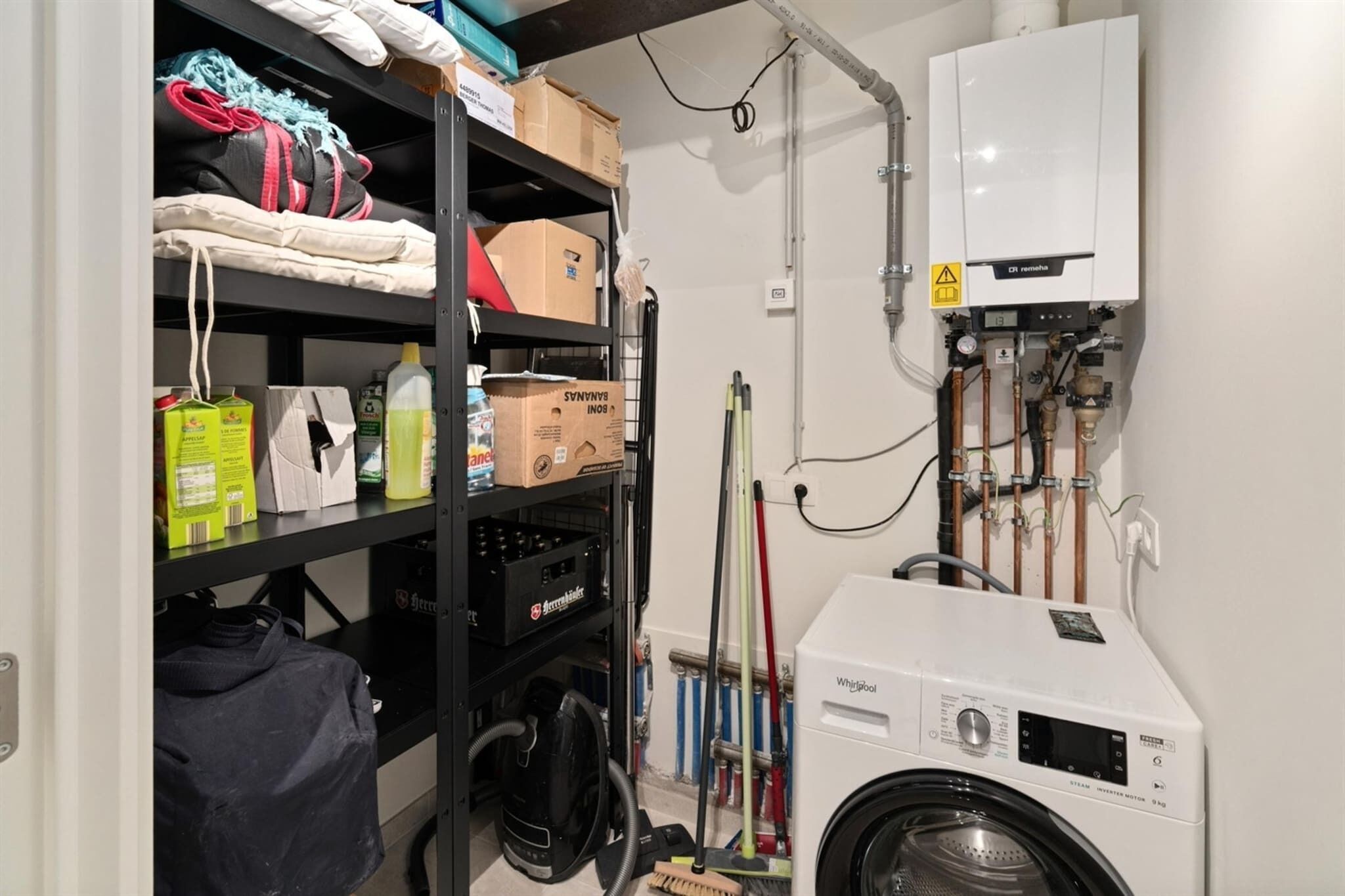 A laundry room with a washing machine, shelves with various items, and a water heater.