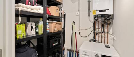 A laundry room with a washing machine, shelves with various items, and a water heater.