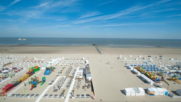 A beach with numerous beach umbrellas and sun loungers, a water slide, and a lifeguard tower. - Flat in Bruges with Panoramic City Views (BLANKENBERGE)