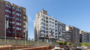A multi-story residential building with balconies, a parking area, and a clear blue sky. - Flat in Bruges with Panoramic City Views (BLANKENBERGE)