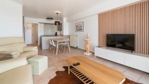 Ein modernes Wohnzimmer mit einer Couch, einem Holztisch, einem Fernseher und einem Essbereich mit Tisch und Stühlen.