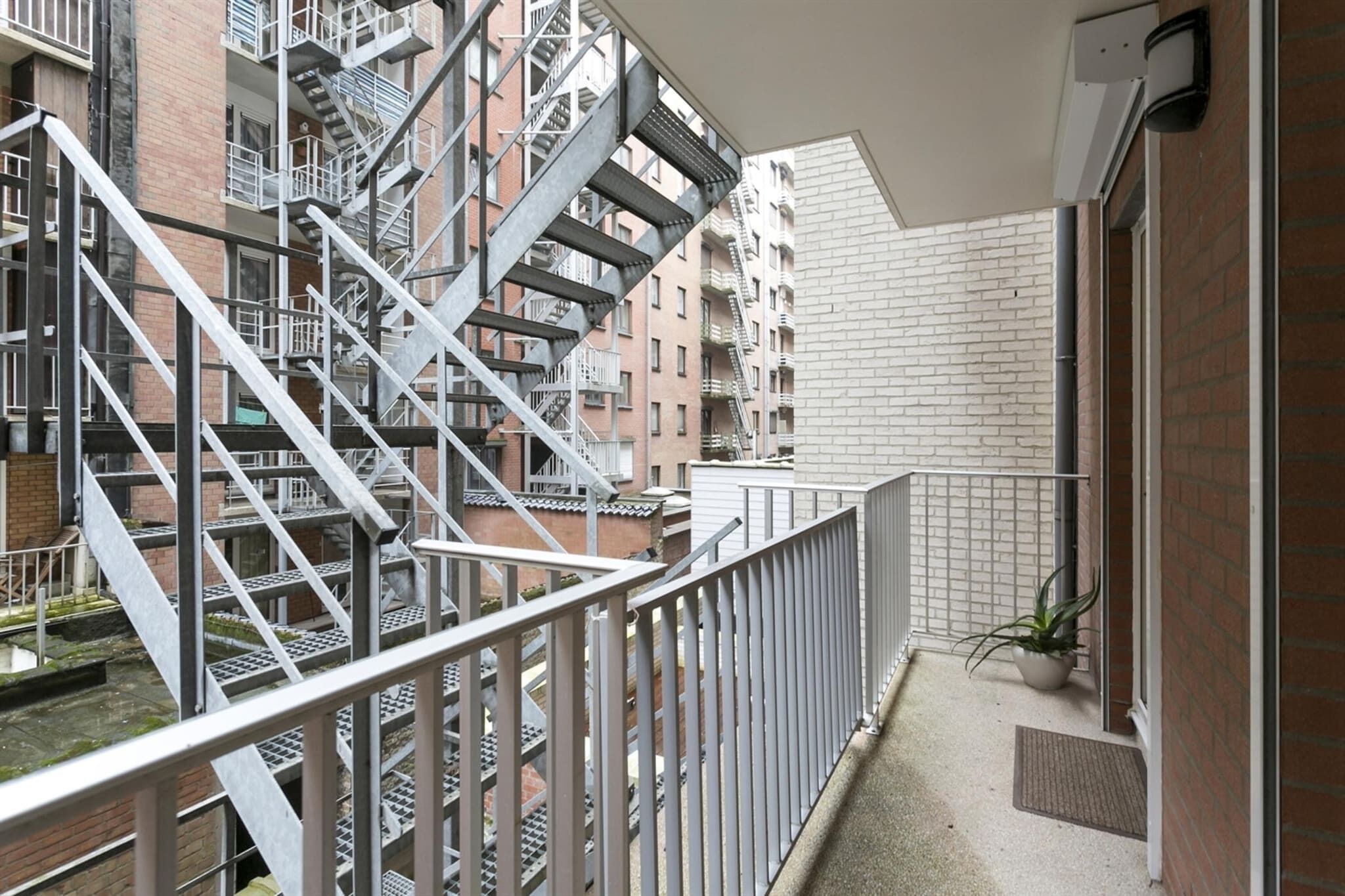 A balcony with a metal railing overlooking a brick building with multiple fire escapes.