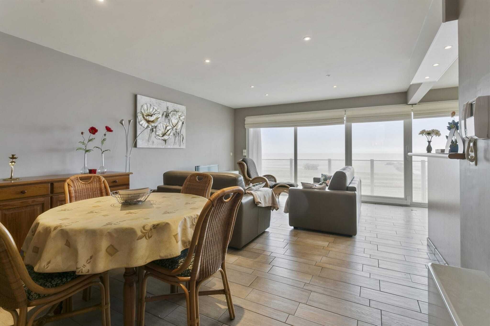 A spacious living area with a dining table, chairs, and a sofa. There is a large window providing a view of the outdoors.