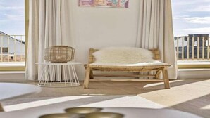 A balcony with a wicker chair, a small round table, and a painting on the wall.