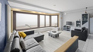 A modern living room with a large window, a sofa, a coffee table, and a TV area.