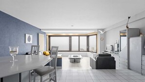 A modern kitchen with a dining area, large windows, and a view of the outdoors.