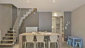 A modern interior with a wooden dining table, four chairs, a staircase with a net, and a small blue table with stools.