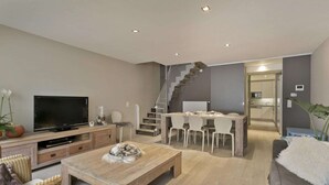 A modern living room with a TV, wooden furniture, a staircase, and a dining area.