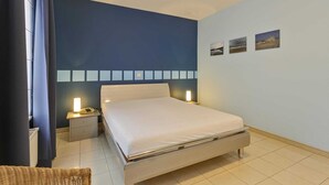 A bedroom with a bed, bedside tables, a nightstand, and wall-mounted lights. - Apartment in Blankenberge near Seafront (BLANKENBERGE)