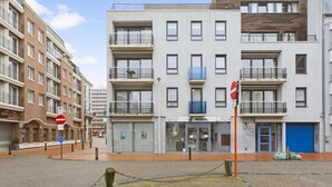 A modern multi-story building with a glass storefront, balconies, and a no-entry sign. - Apartment in Blankenberge near Seafront (BLANKENBERGE)