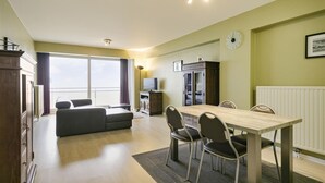 A modern living room with a dining area, a sofa, a TV, and a view of the outside.