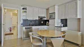 A compact kitchen with white cabinets, a black countertop, stainless steel appliances, and a round dining table with chairs. - Apartment in Blankenberge with Sea Views (BLANKENBERGE)