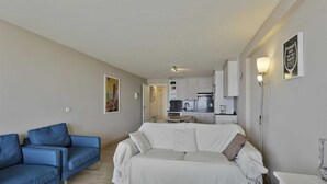 A modern living room with a white sofa and blue armchairs, a kitchen in the background, and a framed quote on the wall. - Apartment in Blankenberge with Sea Views (BLANKENBERGE)