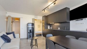 A modern hotel room with a kitchenette, a sofa, a dining table, and a bed. - Studio in Blankenberge with Stunning Sea View (BLANKENBERGE)