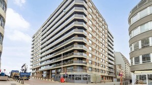 A multi-story residential building with a modern design, featuring balconies on each floor and a ground-level commercial space. - Studio in Blankenberge with Stunning Sea View (BLANKENBERGE)