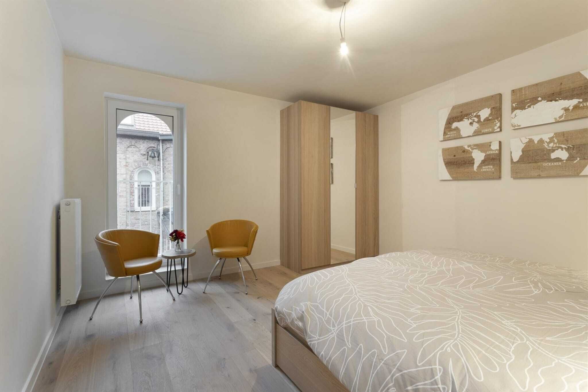 A bedroom with a large bed, two chairs, a small table, and a view of a building through a window.