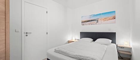 A bedroom with a bed, bedside tables, a nightstand, a door, and a wall-mounted picture.