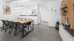 A modern kitchen with a central island, a dining area with a wooden table and black chairs, and a kitchen counter with a black pot and decorative items. - Apartment in Blankenberge with Sea Views (BLANKENBERGE)