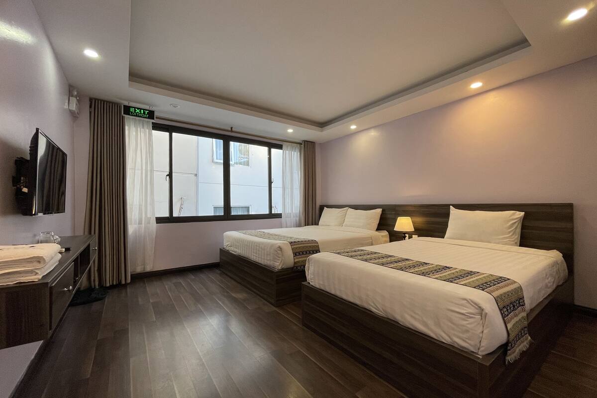 Una habitación de hotel con dos camas, televisión, escritorio y ventana con cortinas.