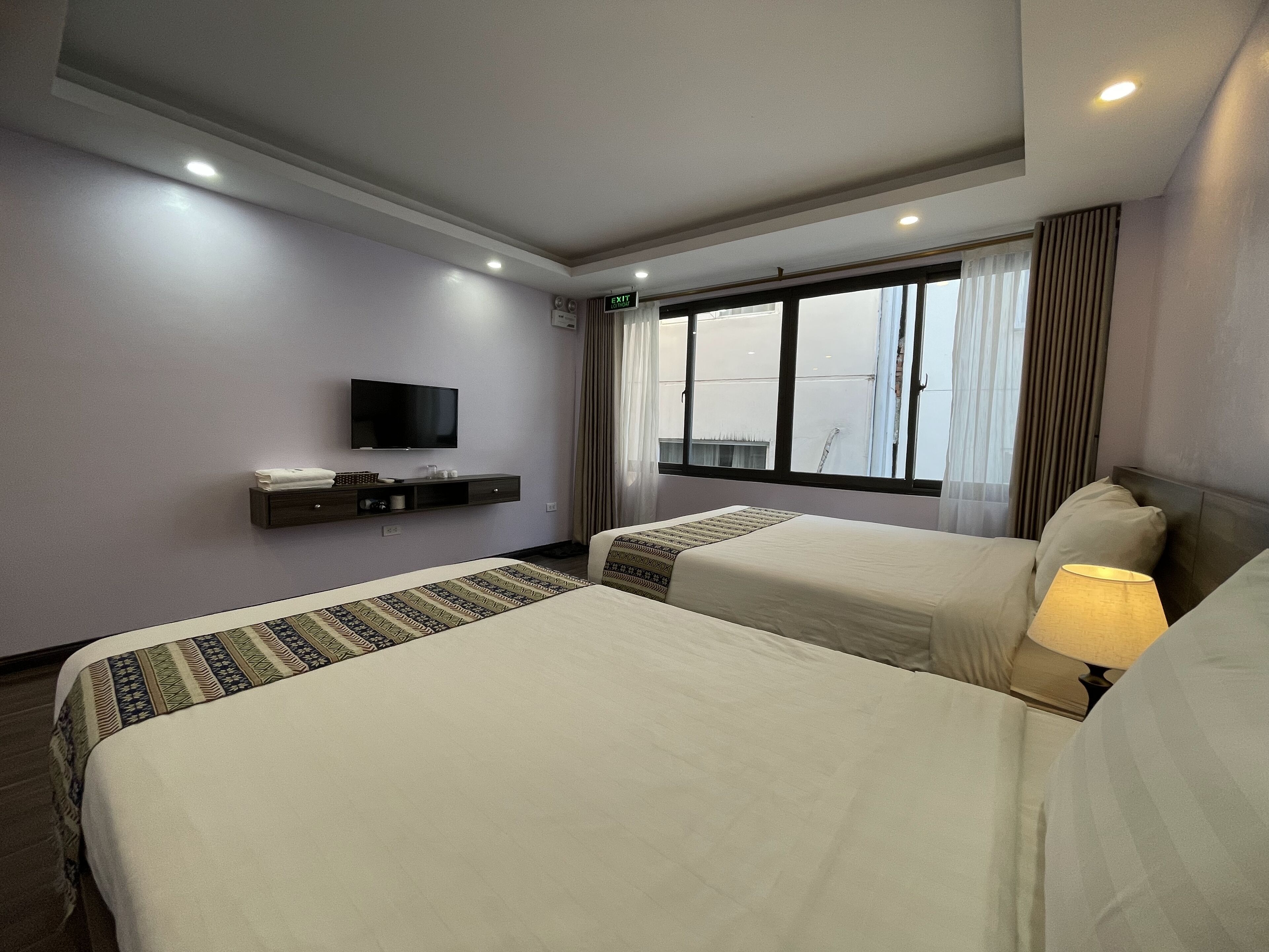 A hotel room with two beds, a flat-screen TV, a window with curtains, and a ceiling light.