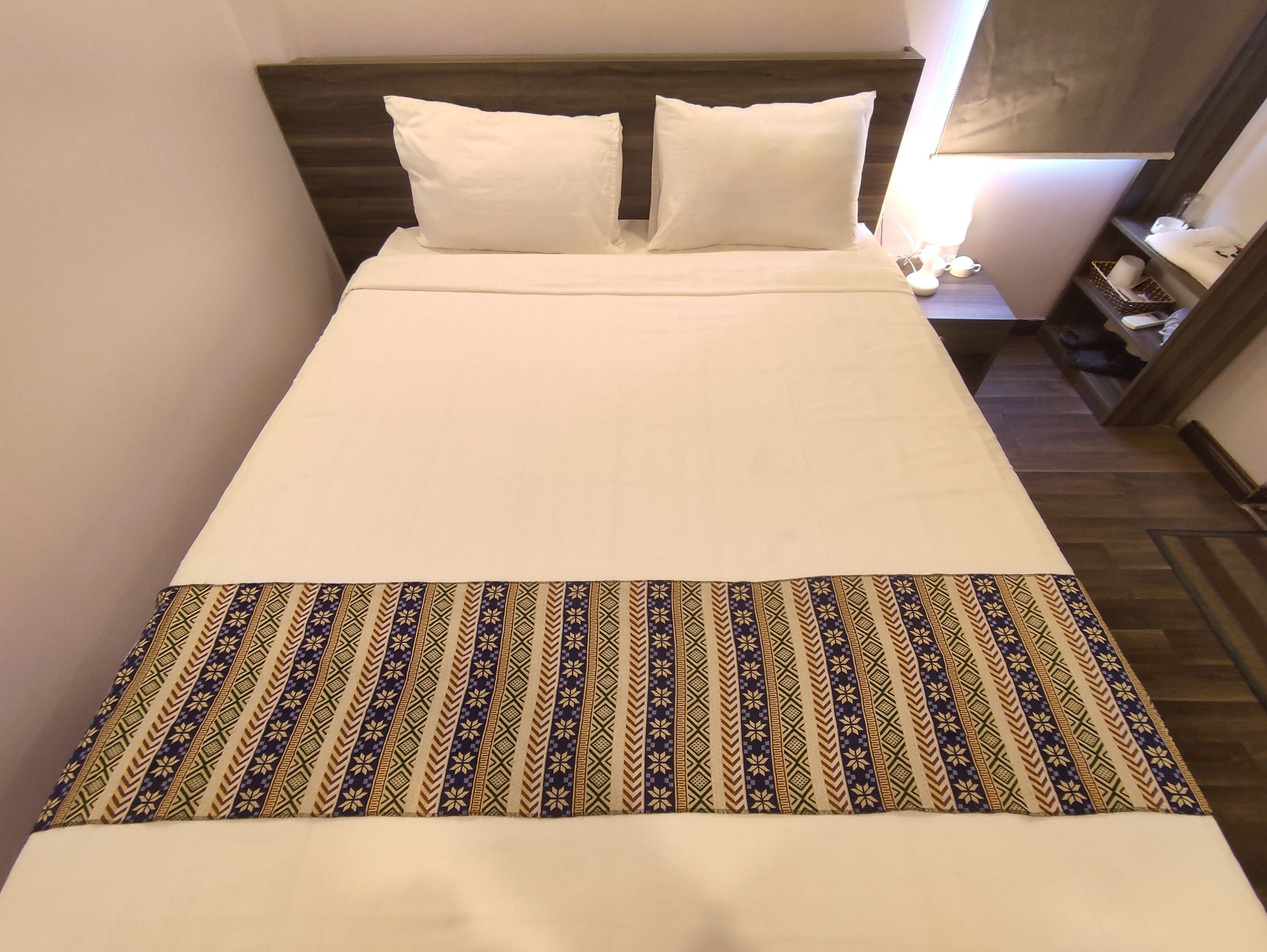 Un lit bien fait, avec du linge de lit blanc et un plaid à motifs.